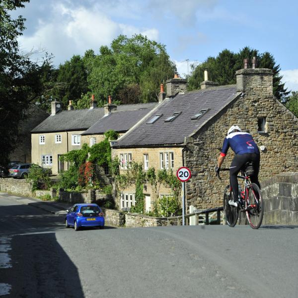 cyclist crossing bridge with cottages in the background